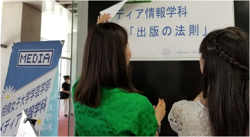 2名の学生がポスターを掲示している様子の写真